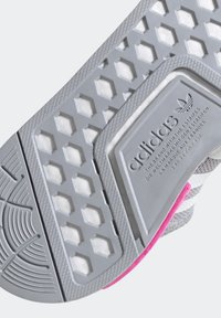 Semelle de chaussure en caoutchouc grise présentant un motif en miel, des accents roses et des zones texturées pour l'adhérence, avec une marque embossée sur un panneau latéral.