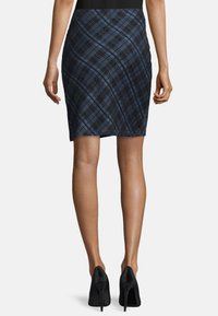 Stickad pennkjol i mörkblått med ett diagonalt rutmönster; figurnära silhuett med en slät yta och svart midjeband, i kombination med svarta klackar.