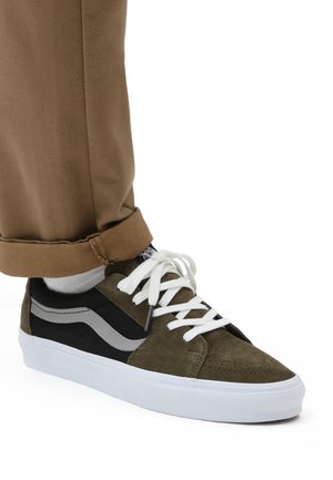 Olivengrønne og sorte sneakers med ruskind og mesh, hvide snørebånd, gummisål og grå side-striber. Bæres med opfoldede khakibukser.