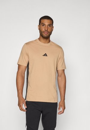 T-shirt de sport beige à manches courtes, col ronde, logo noir sur la poitrine et bandes latérales noires. Tissu doux, coupe ajustée.