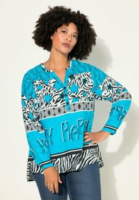 Langearmig shirt met een levendige turquoise basis, zwart-witte dierenprints en een "My Happy" tekstdetail aan de onderrand.