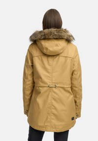 Gul parkajakke med hette foret med pels, innsvingt midje og trykknapplukking ved ermene. Laget av et slitesterkt, vanntett materiale.