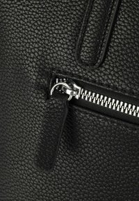 Borsa in pelle nera con texture, dotata di chiusura con zip argentata e linguetta in pelle. Caratterizzata da una superficie in rilievo e linee pulite.