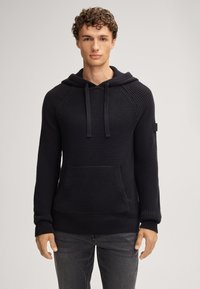 Granatowy dziany hoodie z teksturowanym wzorem, kieszenią kangurzą i regulowanym kapturem. Posiada ściągacze na mankietach i dole dla lepszego dopasowania.