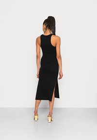 Vestido preto sem mangas com uma silhueta ajustada, comprimento até à metade da panturrilha e fenda lateral. O tecido parece suave com um ligeiro elástico.