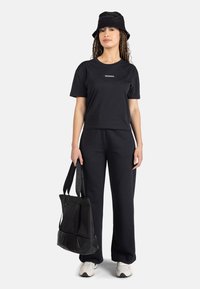 Conjunto de camiseta y pantalones negros, con un pequeño logo. Combinado con un bolso tote negro y un sombrero de cubo, ambos con tela texturizada. Incluye zapatillas.