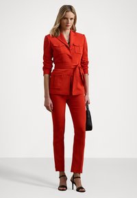Rode op maat gemaakte pak met een getailleerde blazer, twee voorzakken en bijpassende broek. Draagt het met zwarte bandjeshakken en een kleine zwarte handtas.