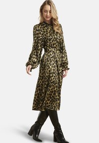 Vestito in raso verde oliva con stampa leopardata, maniche lunghe, cintura in vita e lunghezza midi fluida, abbinato a stivali neri al ginocchio.