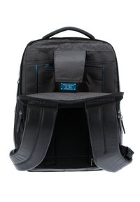 Mochila negra con correas ajustables, que cuenta con un interior amplio, múltiples bolsillos y un acabado texturizado. El hardware incluye cremalleras y marcas.