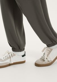 Grå joggers med elastiska manschetter, kombinerade med vita och beige sneakers som har en mörkgrön accent och texturerade detaljer i sulan.
