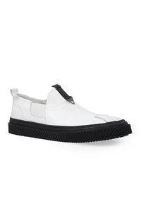Weiße Leder-Slipper mit schwarzer Gummisohle, ausgestattet mit strukturiertem Profil, elastischen Seitenpaneelen und einem dekorativen schwarzen Riemen.