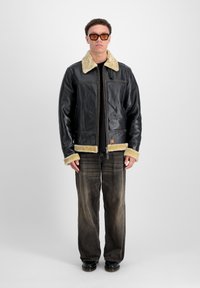 Jachetă neagră din piele cu guler și manșete din blană bej, fermoar frontal și două buzunare laterale. Purtați cu blugi negri decolorati și pantofi negri.