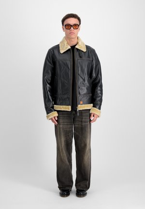 Zwarte leren jack met een beige schapenvacht kraag en manchetten, vofront rits en twee zijzakken. Draag het met vervaagde donkere jeans en zwarte schoenen.