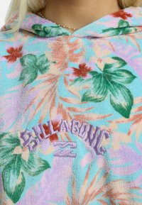 Sudadera con capucha de forro polar azul pastel con un patrón floral tropical en verde, coral y rosa. "BILLABONG" bordado en letras moradas en forma curva.