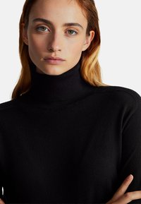 Czarny sweter typu golf wyk made z dzianiny, o dopasowanym kroju i gładkiej teksturze, z czystymi liniami i bez widocznych wzorów.