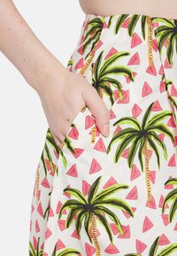Tiskana krilna obleka z motivom palm in roza trikotnikov na beli podlagi, s vidno stransko žepom in gladko teksturo.