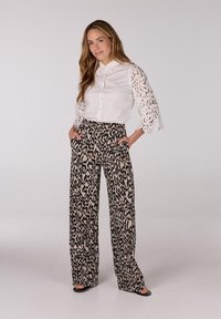 Witte blouse met kantmouwen, gecombineerd met wijde leopardprintbroeken. De broeken hebben zakken en een neutraal kleurenpalet.