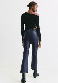 Czarny dopasowany top z długim rękawem i aniolskim dekoltem; zestawiony z granatowymi, sztucznymi skórzanymi spodniami dzwonami. Wyróżnia się gładką fakturą i subtelnymi szwami.