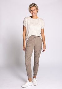 Hellbeiges Grafik-T-Shirt mit kurzen Ärmeln, kombiniert mit beigen Cargohosen mit Seitentaschen und enganliegenden Bündchen, getragen mit weißen Turnschuhen.