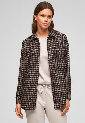 Schwarz-rosa karierte Jacke mit Kragen, Knopfverschluss und langen Ärmeln, aus gewebtem Stoff. Über einem hellen Oberteil und einer Hose getragen.