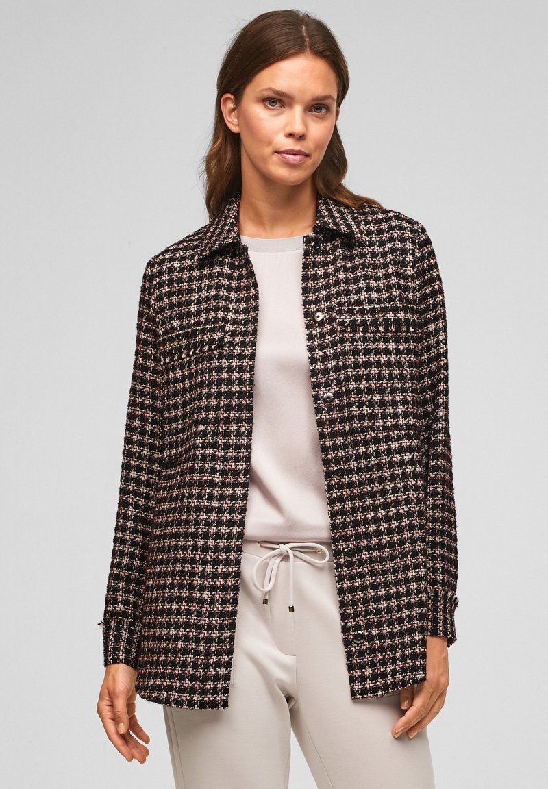 Schwarz-rosa karierte Jacke mit Kragen, Knopfverschluss und langen Ärmeln, aus gewebtem Stoff. Über einem hellen Oberteil und einer Hose getragen.