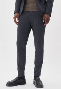 Dunkelgraue maßgeschneiderte Hose aus strukturiertem Stoff, schmal geschnitten, mit Seitentaschen, kombiniert mit schwarzen Lederloafers und einem braunen Pullover.