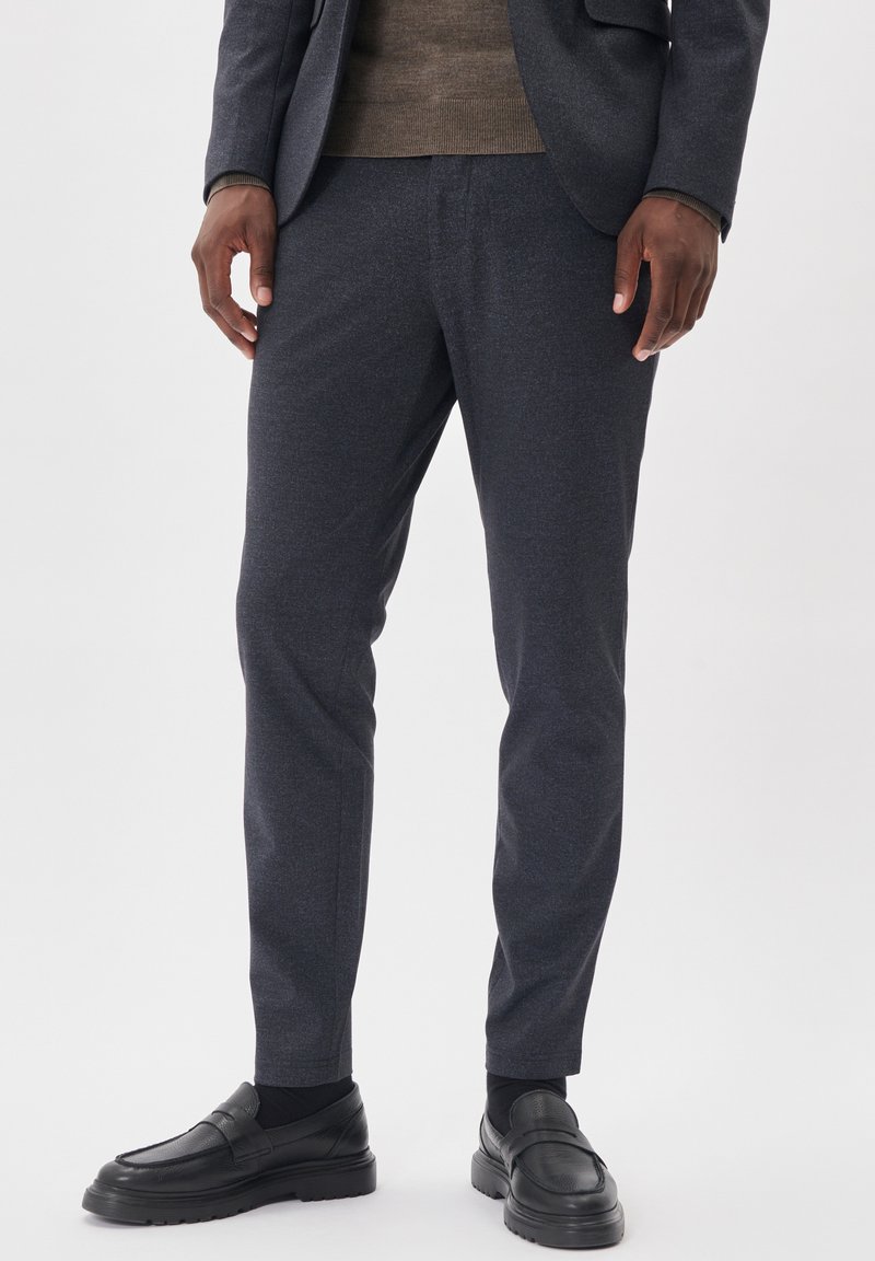 Dunkelgraue maßgeschneiderte Hose aus strukturiertem Stoff, schmal geschnitten, mit Seitentaschen, kombiniert mit schwarzen Lederloafers und einem braunen Pullover.