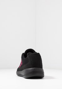 Sort atletiksko med tekstureret overflade, pink logo-detalje, mesh-accenter og en gummisål, set bagfra.