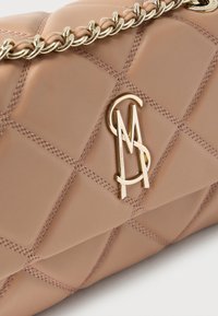 Μπεζ καπιτονέ δερμάτινη τσάντα με χρυσή αλυσίδα λουρί και χρυσά αρχικά λογότυπο "SM" στην μπροστινή πτέρυγα.