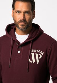 Felpa con cappuccio color marsala, con logo ricamato "HERITAGE JP" bianco, dettagli con bottoni, cappuccio regolabile e texture morbida, caratterizzata da una vestibilità casual.