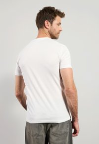 T-shirt en coton blanc avec un col rond et des manches courtes, vu de l'arrière. Texture lisse et coupe standard.