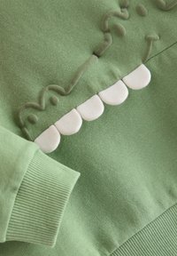 Πράσινο φούτερ με ριμπ μανσέτες, με ανάγλυφα λευκά δόντια και σχέδιο χαμόγελου. Μαλακή υφή, άνετη εφαρμογή.