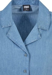 Light blue denim shirt with collar and two buttons visible, showing Urban Classics brand label and size XS, made in Pakistan.