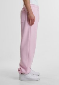 Lys rosa joggebukser med en innsnevring design, elastiske mansjetter og sidelommer, kombinert med hvite sneakers på en ensfarget bakgrunn.