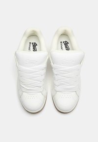 Weiße Sportschuhe mit einem glatten Lederobermaterial, runder Zehenpartie, dicken Schnürsenkeln und Belüftungsperforationen. Gummisohle mit strukturiertem Grip.