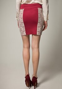 Jupe rouge avec des panneaux latéraux en dentelle blanche, design ajusté et taille large. Le matériau est doux, avec une texture lisse et une coupe droite.
