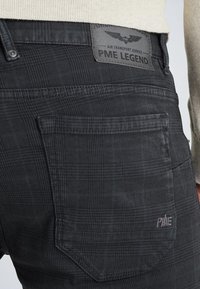 Svart rutiga byxor med en strukturerad tyg och en bakficka samt PME Legend-läderpatch. Diskreta blå accenter i mönstret.