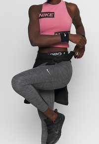 Top corto rosa de Nike con logo negro, leggins grises con acentos laterales y zapatillas deportivas negras. Una pulsera negra completa el conjunto.