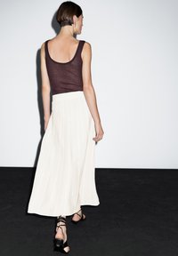 Burgundy ribbed tank top paired with a flowy white pleated maxi skirt, complemented by strappy black heels. Simple and elegant design.