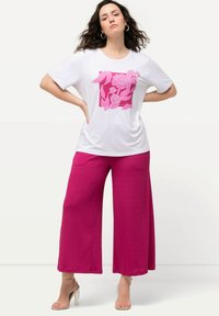 T-shirt bianco a maniche corte con grafica floreale rosa e design quadrato, abbinato a pantaloni rosa a gamba larga. Tessuto liscio, vestibilità comoda.