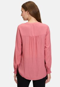 Lys rosa bluse med lange ærmer, rund halsudskæring, samlet detalje bagtil og elastiske manchetter. Blød tekstur og afslappet pasform.