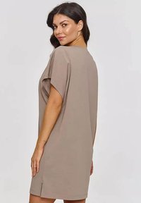 Przeciążona beżowa sukienka t-shirt z miękkiego materiału. Krótkie rękawy, luźny krój, boczne rozcięcia i okrągły dekolt zwiększają wygodę i wentylację.