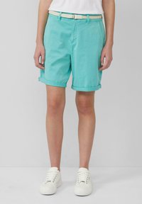 Turquoise korte broek met een geweven witte riem, voorzien van voorzakken en een relaxed fit. Gecombineerd met witte sneakers.