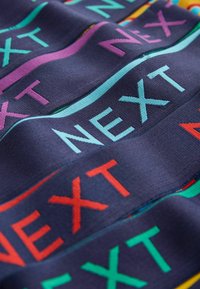 Țesătură albastru închis cu dungi colorate, prezentând cuvântul „NEXT” scris diagonal, în culori roșu, turcoaz, violet și verde.