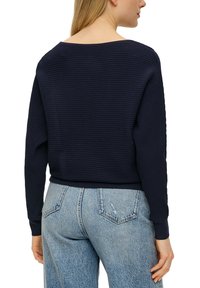 Marineblauer gerippter Strickpullover mit weitem Ausschnitt, abfallenden Schultern und enganliegenden Bündchen, kombiniert mit hellblauen hochtaillierten Jeans.