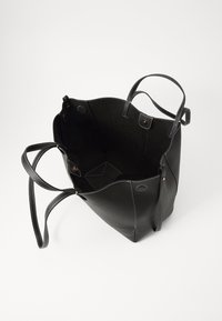 Sac cabas en cuir noir avec une surface texturée, ouverture supérieure, deux poignées et des coutures de couleur claire. L'intérieur semble spacieux et doublé.