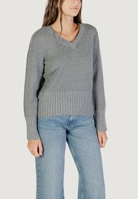 Maglione grigio a maglia con scollo a V, polsini e fondo a costine. Abbinato a jeans a gamba larga di colore blu chiaro. Texture liscia, design casual.