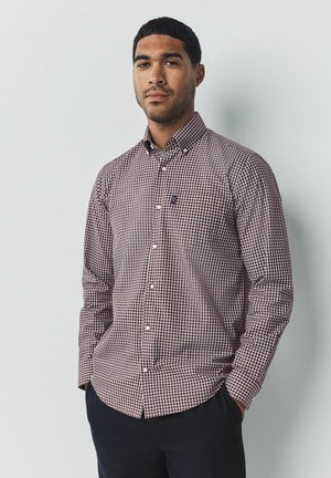 Een overhemd met een klein ruitpatroon in bordeauxrood en wit, lange mouwen en een button-down kraag, gecombineerd met donkere broek.