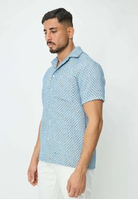 Chemise à manches courtes bleu clair avec un motif géométrique, fabriquée dans un tissu respirant, dotée d'un col et d'une poche poitrine.