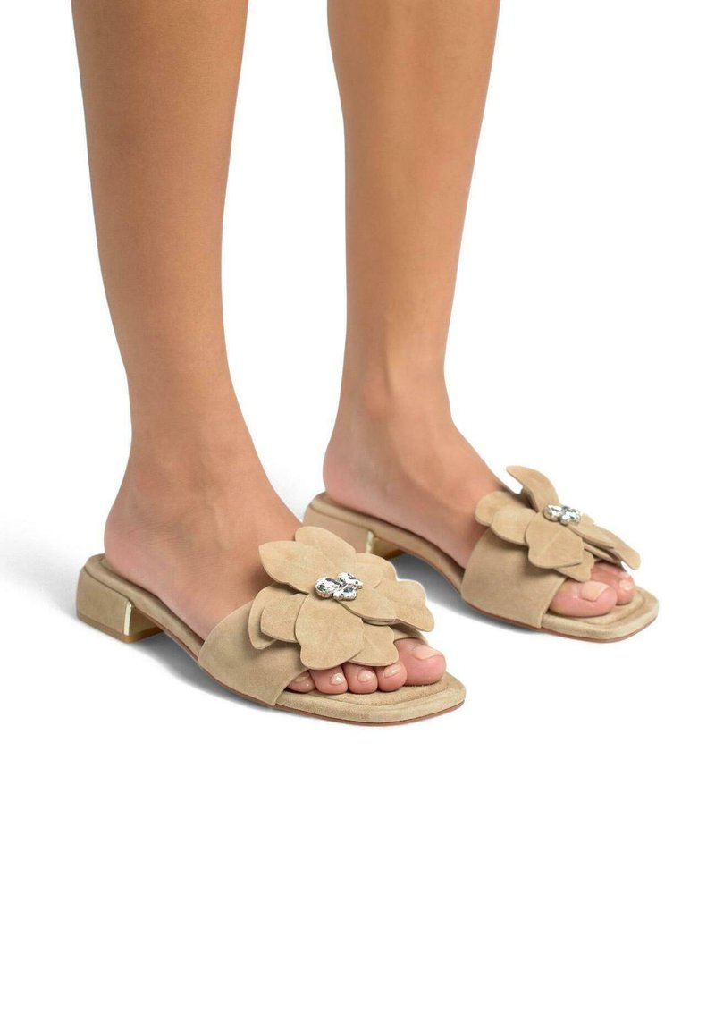Sandales à glissière en suède beige présentant un grand motif floral avec des pétales superposés et un centre décoratif en rhinestones, talon bas.